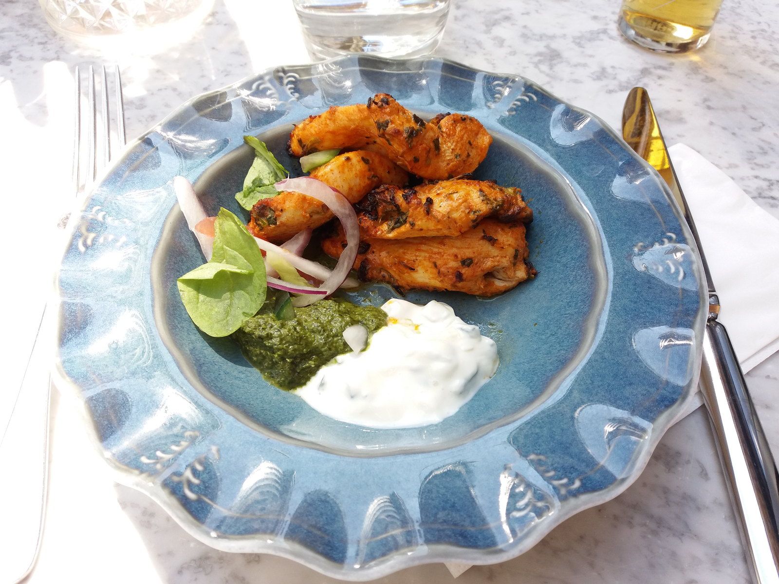 Chicken tikka on a blue plate with onion, lime and mint chutney