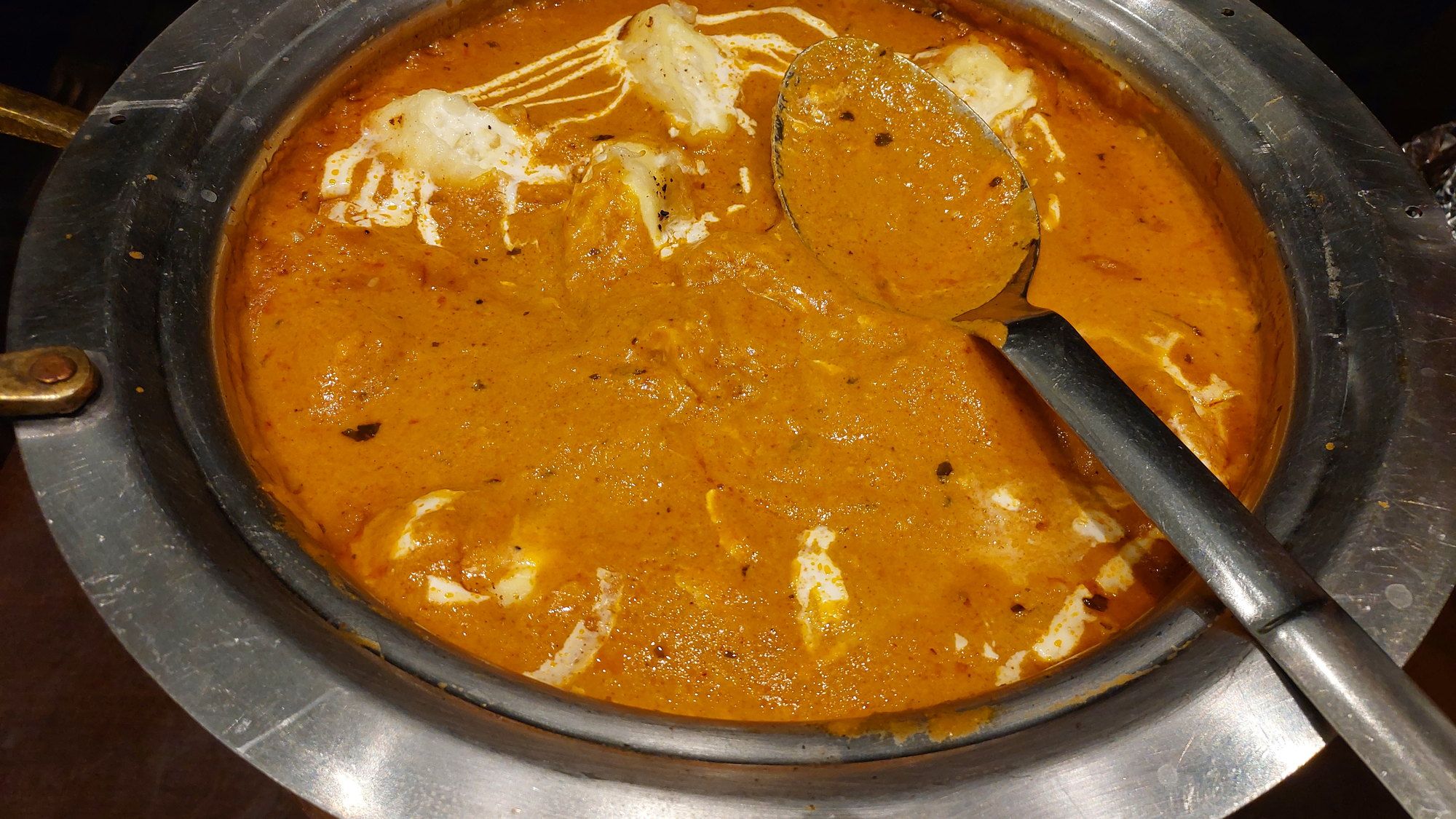 Paneer simmering in a glossy orange butter-masala gravy in a steel karahi